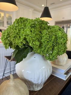 a white vase filled with green leaves on top of a table next to a lamp