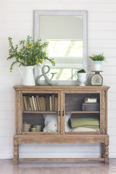 an old wooden cabinet with books and plants on top is displayed in front of a mirror