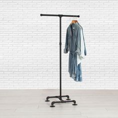 a coat rack with clothes hanging on it in front of a white brick wall and floor