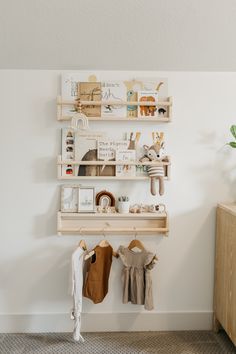 two wooden shelves with clothes hanging on them and a potted plant in the corner