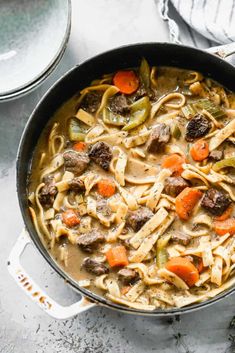 a skillet filled with pasta and beef stew on top of a white countertop