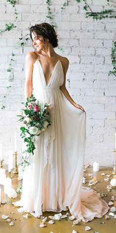 a woman standing in front of a white brick wall with flowers and greenery on it