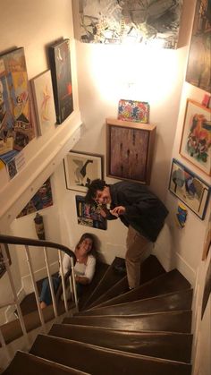 two people are standing on the stairs in a room with pictures and paintings above them