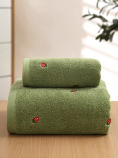 two green towels with strawberrys on them sitting on a table next to a potted plant