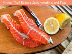 two pieces of fish on a cutting board with lemons and a knife next to it