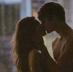 a man and woman kissing in front of a window with the city lights behind them