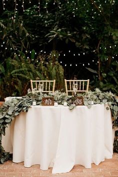 the table is set up with white linens and greenery for an elegant look