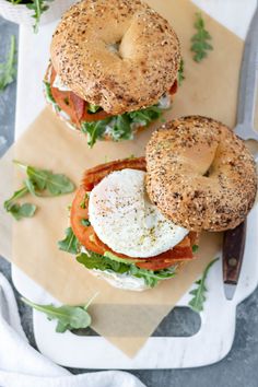 two bagels with bacon, lettuce and tomato on them sitting on a cutting board