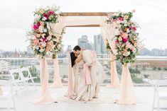 two people kissing under an arch decorated with flowers and greenery on top of a roof