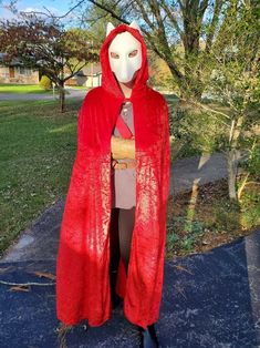 a person wearing a red cape and mask standing on a sidewalk in front of a tree