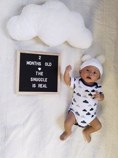 a baby laying next to a sign that says 2 months old the snuggle is real