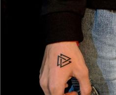 a person's hand with a small triangle tattoo on their left thumb and finger