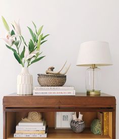 a wooden table topped with books next to a lamp and a vase filled with flowers