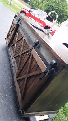 a large wooden box sitting on the side of a road next to a red car