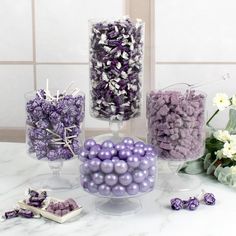 purple and white candies in glass vases on marble counter top next to flowers