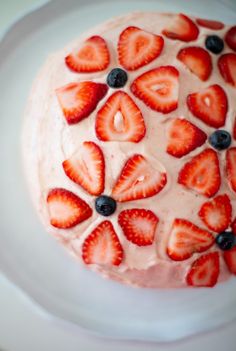 a white plate topped with a cake covered in strawberries and blueberries on top of it