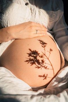 a pregnant woman's belly with the shadow of a plant on it, while lying in bed