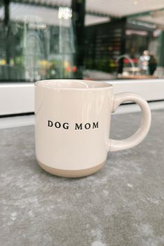 a white coffee mug with the words dog mom on it sitting on a table in front of a store window