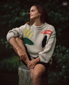 a woman sitting on top of a tree stump wearing a sweater with flowers and leaves