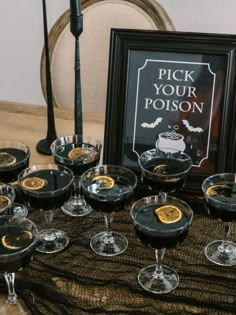 a table topped with lots of glasses filled with liquid next to a framed halloween sign