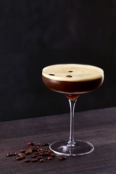 a glass filled with liquid sitting on top of a wooden table next to coffee beans