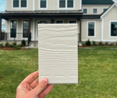 a hand is holding up a piece of white paper in front of a large house