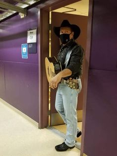 a man wearing a cowboy hat and bandana holding a guitar in front of a purple wall