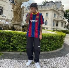 a man with dreadlocks standing in front of a fountain wearing a soccer shirt