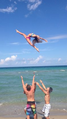 two people jumping in the air at the beach while another person watches from the shore