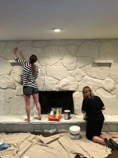 two women are painting a stone fireplace in a room with no one on the mantle