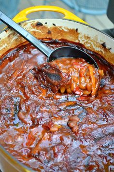 a pot full of beans and meat with a ladle scooping some food out