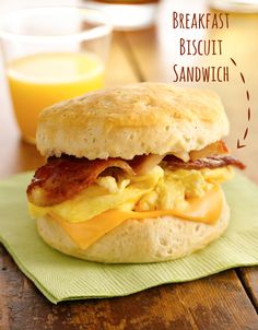 a bacon, egg and cheese biscuit sandwich on a green napkin next to a glass of orange juice