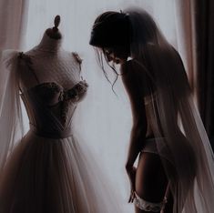 a woman standing next to a dress on a mannequin in front of a window