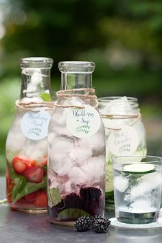 three mason jars filled with ice and berries on top of a table next to two glasses