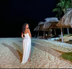 a woman in a white dress standing on the beach at night with thatched umbrellas