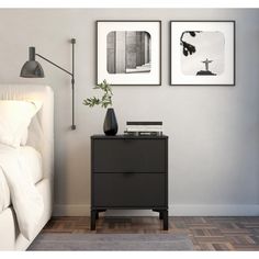 a nightstand with two pictures on the wall above it