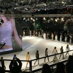 people are walking on the runway at a fashion show in front of a large screen