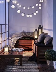 a balcony with lights strung from the ceiling and wooden furniture on the floor, along with potted plants