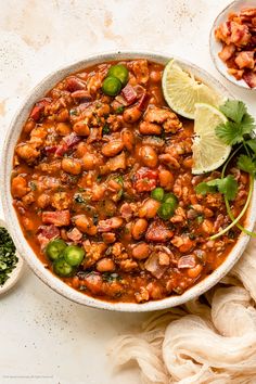 a white bowl filled with chili and beans next to a lime slice on the side