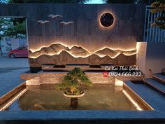 an outdoor fountain in front of a building with mountains on the wall and lights around it