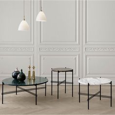 three black and white tables with marble tops in an empty room next to two vases