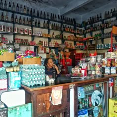 a woman standing behind a counter in a store with lots of bottles on the shelves