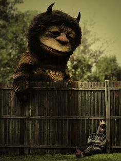 a man sitting in the grass next to a fence with an animal on top of it