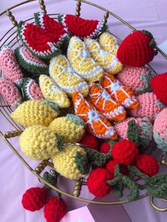 crocheted fruits and vegetables are on display in a wire basket next to a pink table cloth