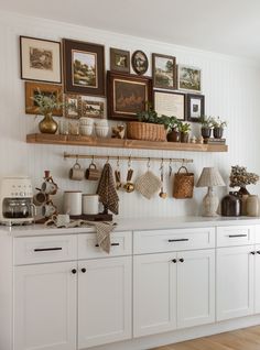 a kitchen with white cabinets and pictures on the wall over the stove, pots and pans