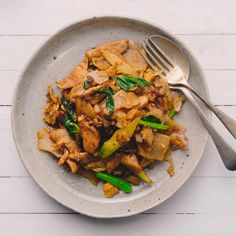 a white plate topped with meat and veggies next to a fork on top of a wooden table