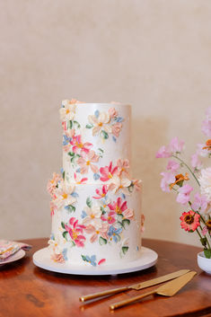 a three tiered white cake with colorful flowers on it and gold utensils