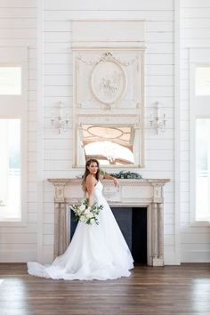 a woman in a white wedding dress standing next to a fireplace