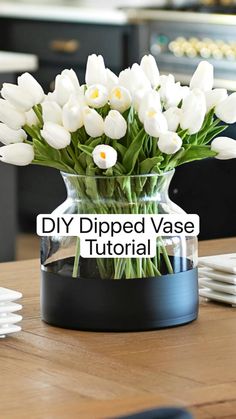 a vase filled with white tulips sitting on top of a wooden table next to plates