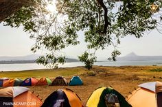 many tents are set up on the ground by the water and some mountains in the distance